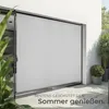 An outdoor scene with a large white roller blind covering a glass door or window, with plants in the foreground and background. Náhled obrázku produktu