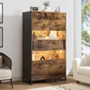 A tall cabinet with LED lighting is displayed in a living room setting, next to a sofa and chair. Produktbild-Vorschau
