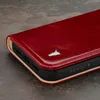 Close-up of a red leather iPhone case with a cutout logo and embossed brand name. Produktbild-Vorschau