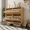 A wooden shoe cabinet with multiple flip-down drawers filled with shoes, placed in a room with a plant and artwork. Produktbild-Vorschau