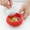 A person is holding a lid over a red bowl containing food, likely eggs and herbs. Podgląd zdjęcia produktu