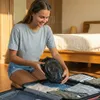 A young woman is packing a snorkel mask into a suitcase in a bedroom. Podgląd zdjęcia produktu