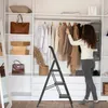 A woman is using a step ladder to organize clothes in a closet. Náhled obrázku produktu