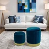 A living room scene with a white sofa, abstract art, and two blue poufs in the foreground. Náhľad obrázku produktu
