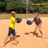 Two children playing with punching bags on a sand court with a volleyball net in the background. Produktbild-Vorschau