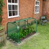 A mini greenhouse with plants inside, placed next to a brick house with windows. Podgląd zdjęcia produktu