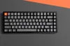 A black mechanical keyboard with gray and orange keys is shown from a top-down perspective on a gray surface with an orange diagonal stripe in the background. Produktbild-Vorschau
