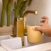 A child's hand is holding a yellow cup under a golden toy faucet, collecting water. Podgląd zdjęcia produktu