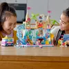 Two young girls are playing with a LEGO Friends water park set on a wooden table. Produktbild-Vorschau