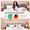 A woman is sitting in a bed covered with a duvet, and below that, hands are raised from under a duvet, holding a mug and making a peace sign. Produktbild-Vorschau
