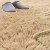 A close-up view of a fluffy beige rug with a pair of gray slippers on it. Produktbild-Vorschau