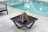 A square fire pit with faux logs sits on a tiled patio next to a swimming pool. Produktbild-Vorschau