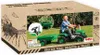 The image shows the packaging of a green pedal tractor with a trailer, featuring a child happily riding the tractor in an outdoor setting. Produktbild-Vorschau