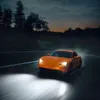 An orange car driving on a wet road at night, with headlights on. Produktbild-Vorschau