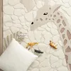 A close-up view of a rug with a giraffe pattern, featuring small toy animals and a pillow. Náhled obrázku produktu