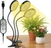 A clip-on LED grow light with three flexible arms is positioned over two potted plants on a wooden desk. Produktbild-Vorschau