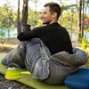 A man sits in a sleeping bag outdoors, holding a cup and looking to the side. Produktbild-Vorschau