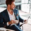 A man in a suit sitting at a table, holding a cup of coffee and reading a newspaper. Produktbild-Vorschau