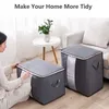 A person is shown putting items into a storage bag. There are two storage bags visible in the image, along with a small table with a plant and a sofa in the background. Produktbild-Vorschau