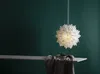 A white paper star lantern hangs in front of a dark green wall, with a shelf and draped fabric in the foreground. Produktbild-Vorschau