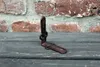 A cast iron shelf bracket is placed on a wooden surface in front of a brick wall. Produktbild-Vorschau