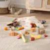 A collection of wooden toy food items arranged on a textured rug, with a stuffed bunny and basket in the background. Produktbild-Vorschau