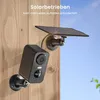 A black security camera with a solar panel attached to a wooden wall, with a blue sky in the background. Náhled obrázku produktu