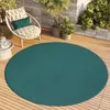 A round teal rug on a wooden deck with a chair and plants. Voir les images du produit