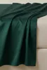 A close-up view of a dark green satin-cotton fitted sheet draped over a light beige surface. Produktbild-Vorschau