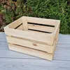 A wooden crate sits on a wooden surface in front of a green hedge. Produktbild-Vorschau