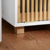 A close-up view of the bottom part of a white cabinet with wooden slatted doors and wooden block feet, resting on a wooden floor. Anteprima dell’immagine prodotto