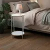 A bedside table with a lamp and a plant next to a bed. Produktbild-Vorschau