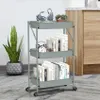 A three-tier rolling cart filled with books and decorative items, placed on a wooden floor next to a potted plant and a cabinet. Voir les images du produit