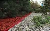 A garden bed border made of red mulch and gray stones, with green plants and trees. Produktbild-Vorschau