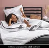 A woman is lying on a bed with pillows and a duvet. The bed has a black headboard. Produktbild-Vorschau