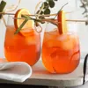 Two glasses of orange-colored drinks with ice and orange slices as garnish, placed on a tray with a white napkin. Náhled obrázku produktu