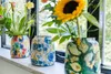 Three decorative vases with floral patterns, filled with flowers, are placed on a windowsill. Voir les images du produit