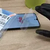 A person in black gloves is applying a screen protector to a smartphone. Produktbild-Vorschau