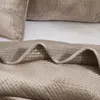A close-up view of a beige quilted blanket folded on a bed. Podgląd zdjęcia produktu
