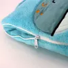 A close-up view of a blue plush blanket with a zipper. The blanket has embroidered details of a cartoon character's face. Produktbild-Vorschau