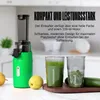 A green juicer is shown on a countertop with two glasses of juice and some fruit and vegetables. Náhled obrázku produktu
