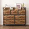 A dresser with seven drawers is shown against a white wall and on a wooden floor. Náhled obrázku produktu