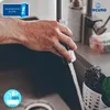 A hand is holding a faucet spray head, with water running into a sink. There are cleaning supplies in a holder on the side. Produktbild-Vorschau