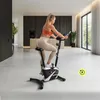 A woman is exercising on a stationary bike in a modern, well-lit room. Produktbild-Vorschau