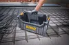 A person's hand wearing a glove is holding a black DeWalt tool box over a grid of rebar on a concrete floor. Podgląd zdjęcia produktu