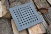 A square cast iron grate with many holes sits on a pile of firewood. Voir les images du produit