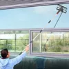 Person in blauem Kapuzenpulli reinigt mit langem Teleskop-Fensterreiniger ein Außenfenster Anteprima dell’immagine prodotto