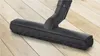 A close-up of a black vacuum cleaner head with bristles on a light wooden floor. Produktbild-Vorschau