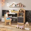 A child is sitting at a desk and reading a book. The desk has shelves and a drawer. There are toys on the floor. Produktbild-Vorschau