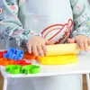 A child's hands are shown using a rolling pin on a yellow playdough mat, surrounded by colorful playdough cutters. Podgląd zdjęcia produktu